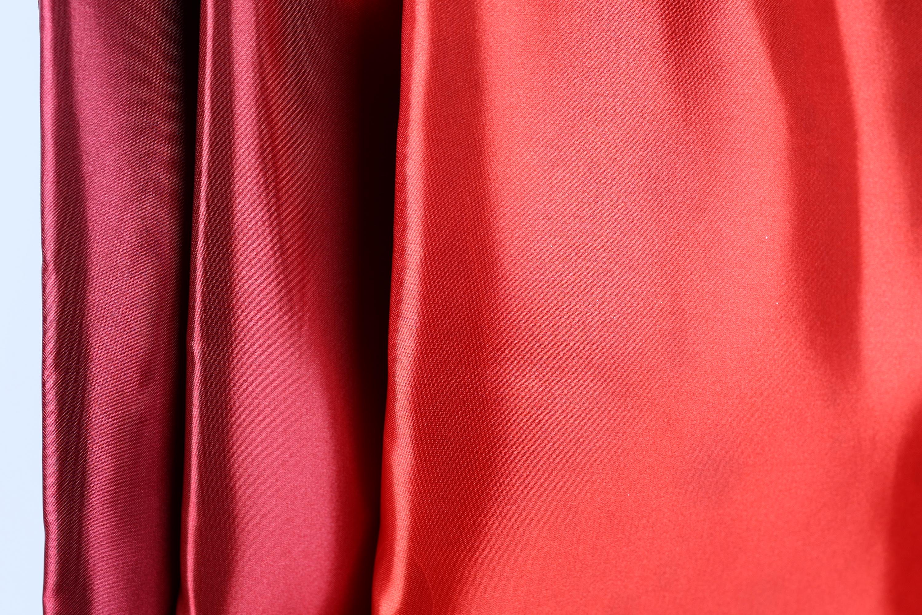 a close-up view of a red fabric, with a red curtain or fabric hanging in the background.