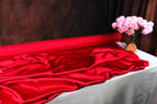 a red fabric draped over a table, with a vase of pink flowers placed next to it.