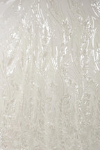 a close-up view of a white fabric with a repeating pattern of thin, wavy lines and leaves. The pattern appears to be made of sequins or glitter, giving the fabric a shiny, textured appearance.