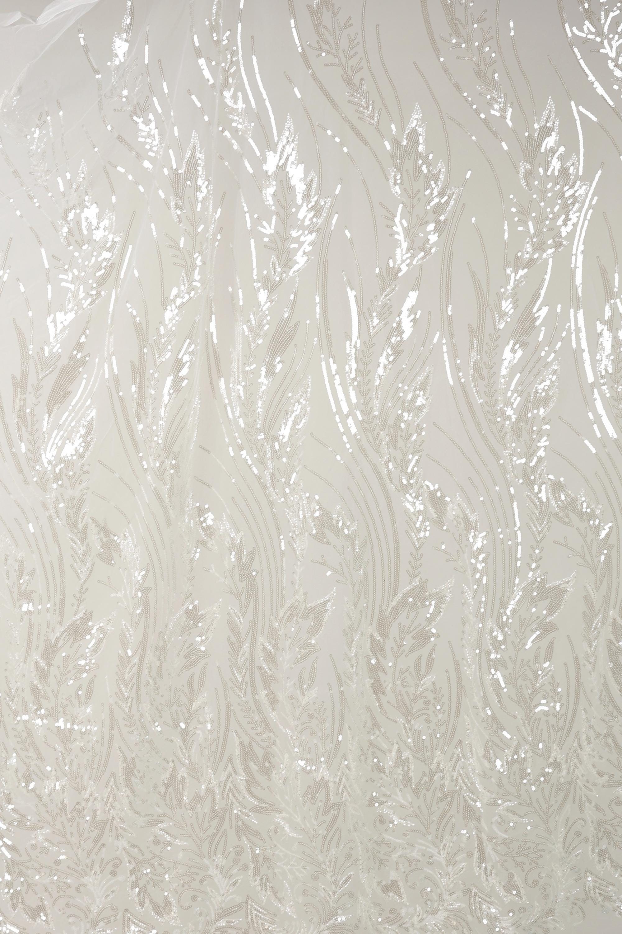a close-up view of a white fabric with a repeating pattern of thin, wavy lines and leaves. The pattern appears to be made of sequins or glitter, giving the fabric a shiny, textured appearance.