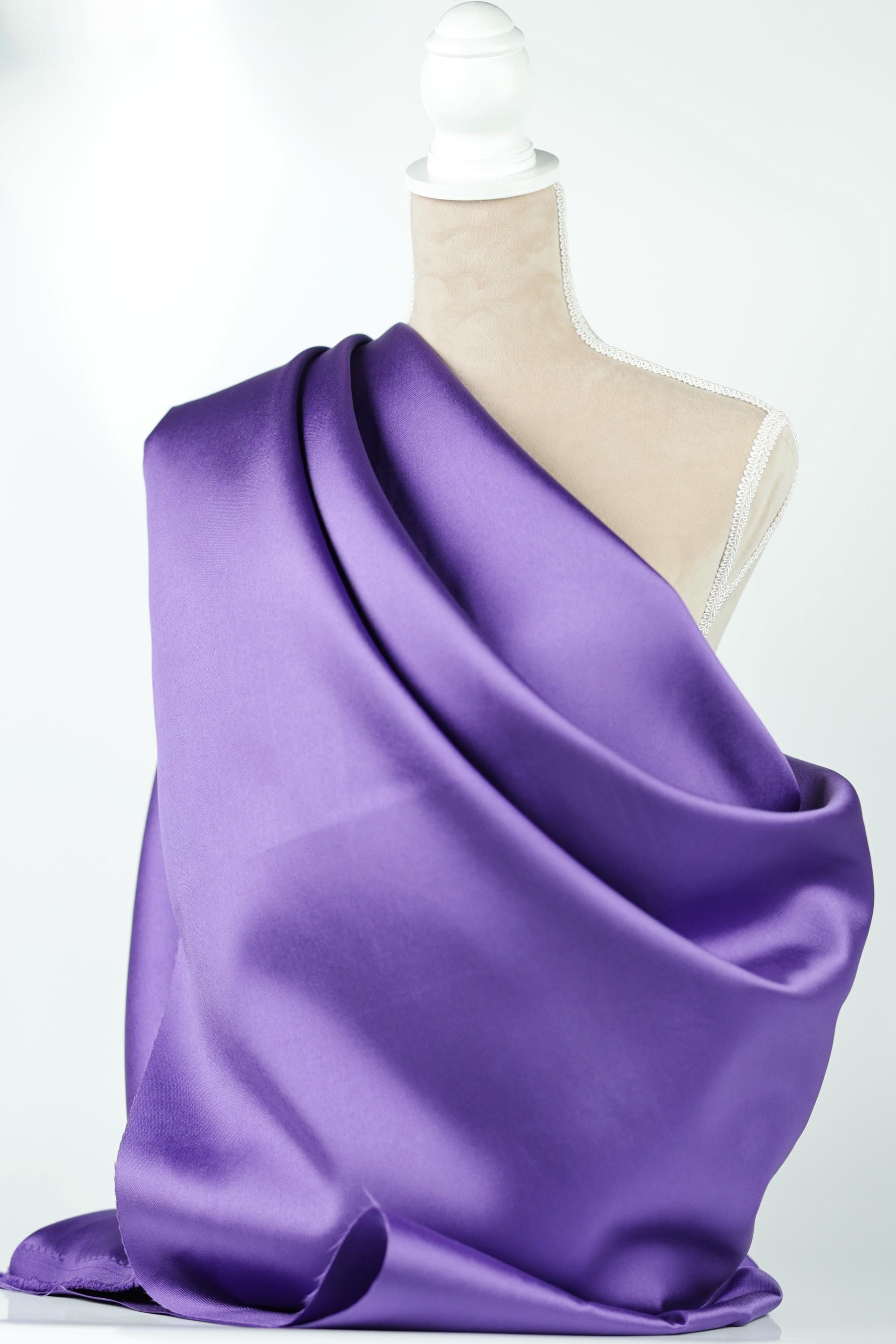 A mannequin is draped in a vibrant purple satin fabric, which is draped over the mannequin's torso.