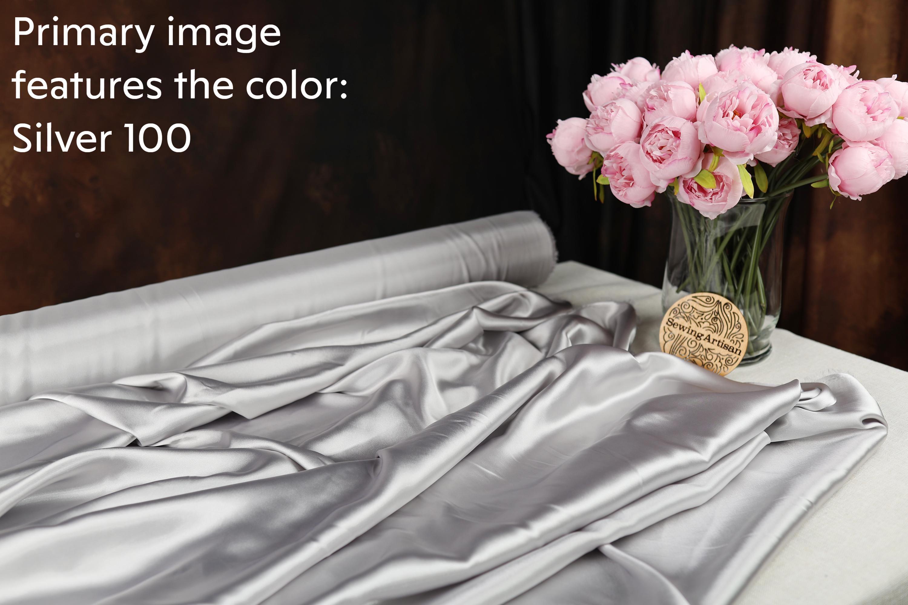 a silver fabric and a vase of pink peonies, with a gold medallion placed on the fabric.