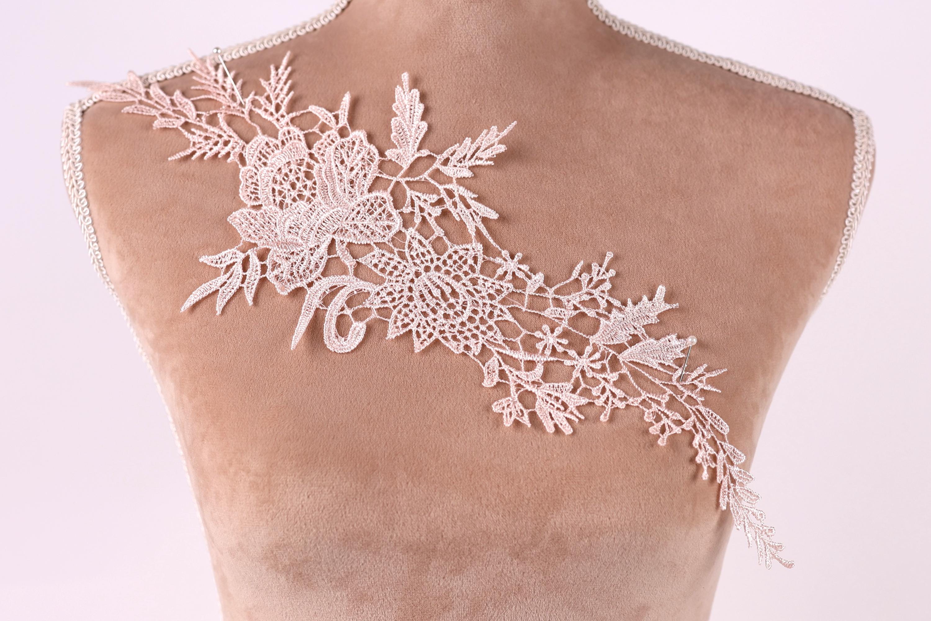 A close-up of a mannequin torso wearing a delicate, intricate lace piece on the shoulder.