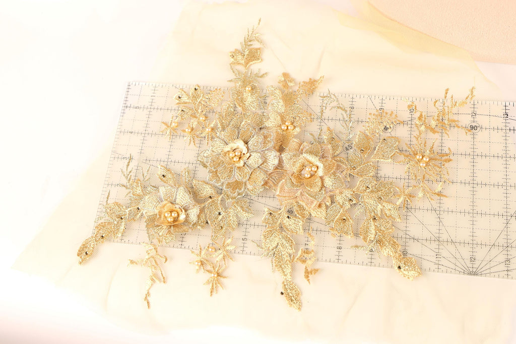 a collection of gold-colored floral embroidery pieces, including flowers and leaves, arranged on a white fabric surface.