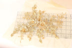 a collection of gold-colored floral embroidery pieces, including flowers and leaves, arranged on a white fabric surface.