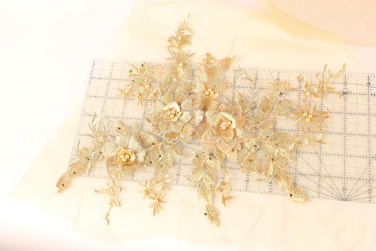 a collection of gold-colored floral embroidery pieces, including flowers and leaves, arranged on a white fabric surface.