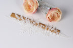 a wooden board with a lace-like design, a clear glass vase with two pink roses, and a wooden stick with a lace-like design.