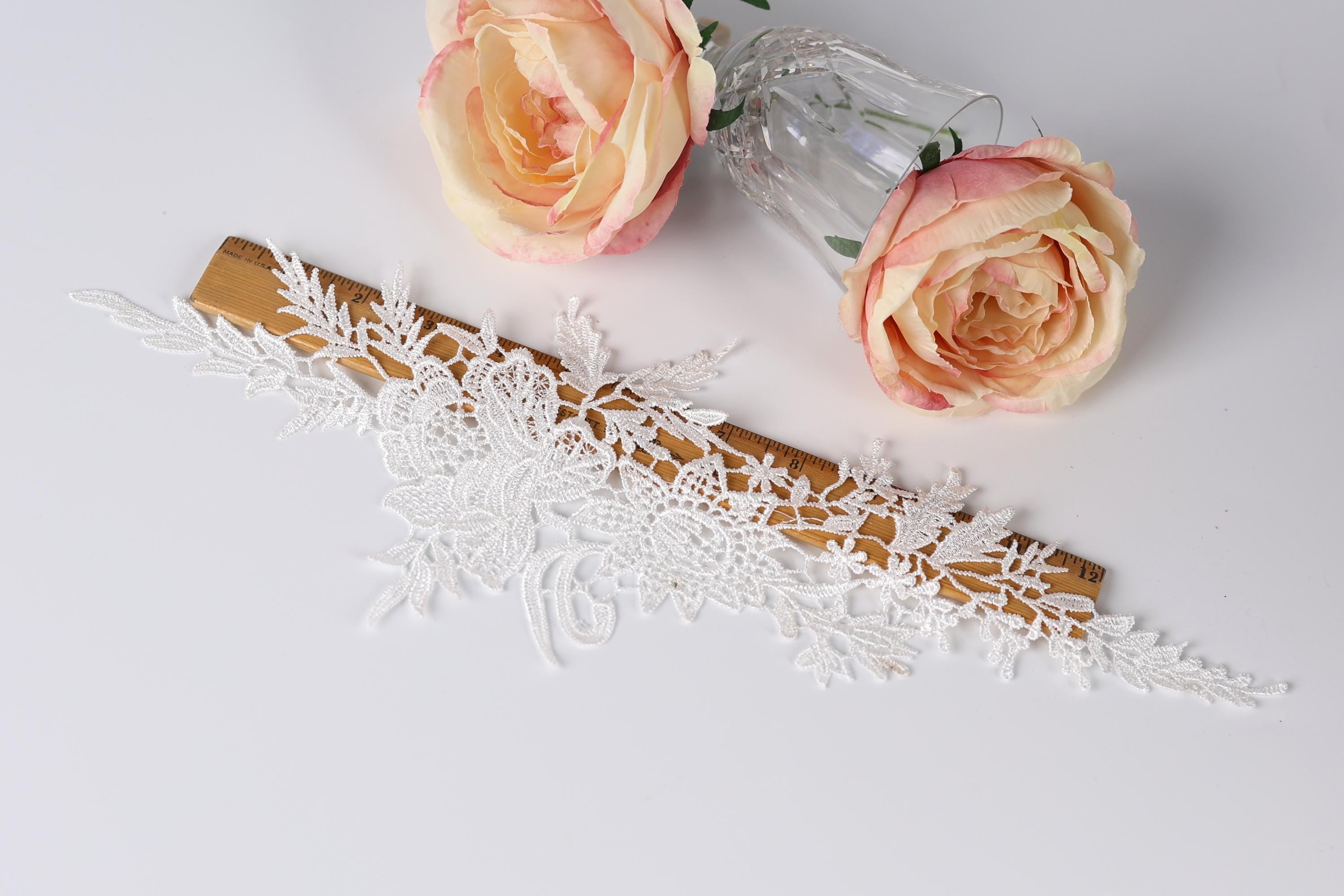 a wooden board with a lace-like design, a clear glass vase with two pink roses, and a wooden stick with a lace-like design.