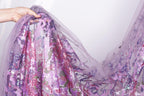 A hand is holding a piece of fabric with a floral pattern in shades of purple and pink.