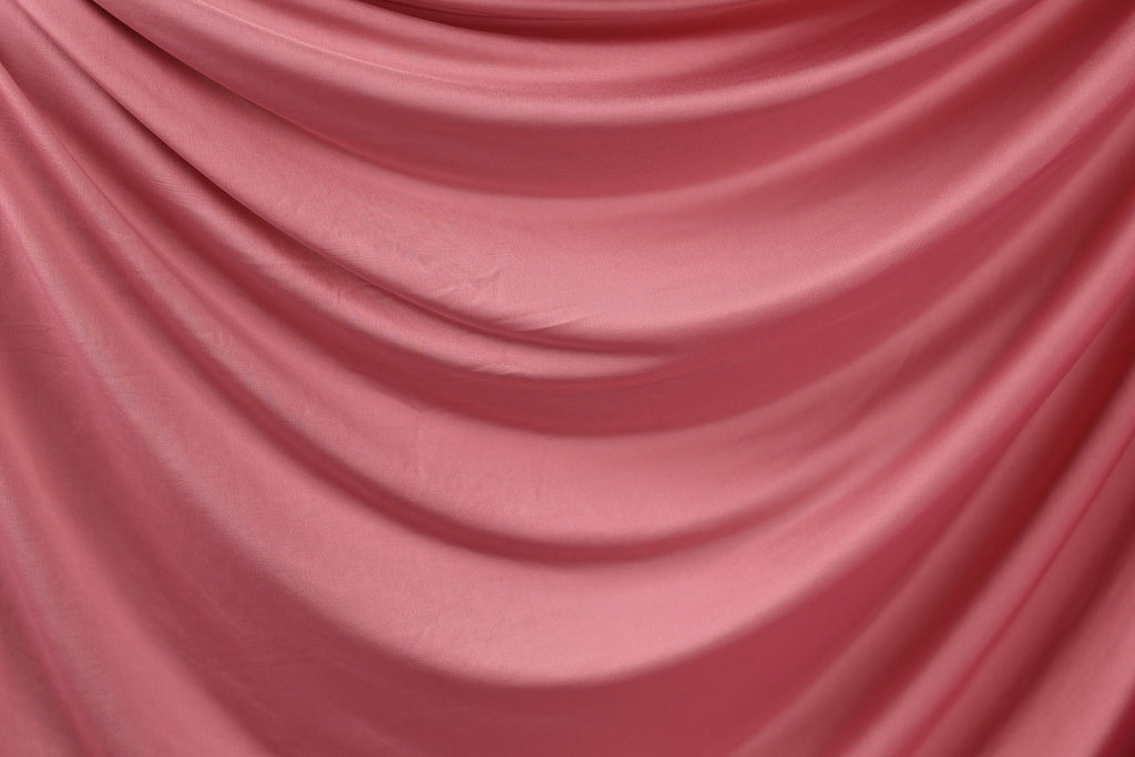 a close-up view of a pink satin fabric, with its folds and creases creating a textured and flowing appearance.