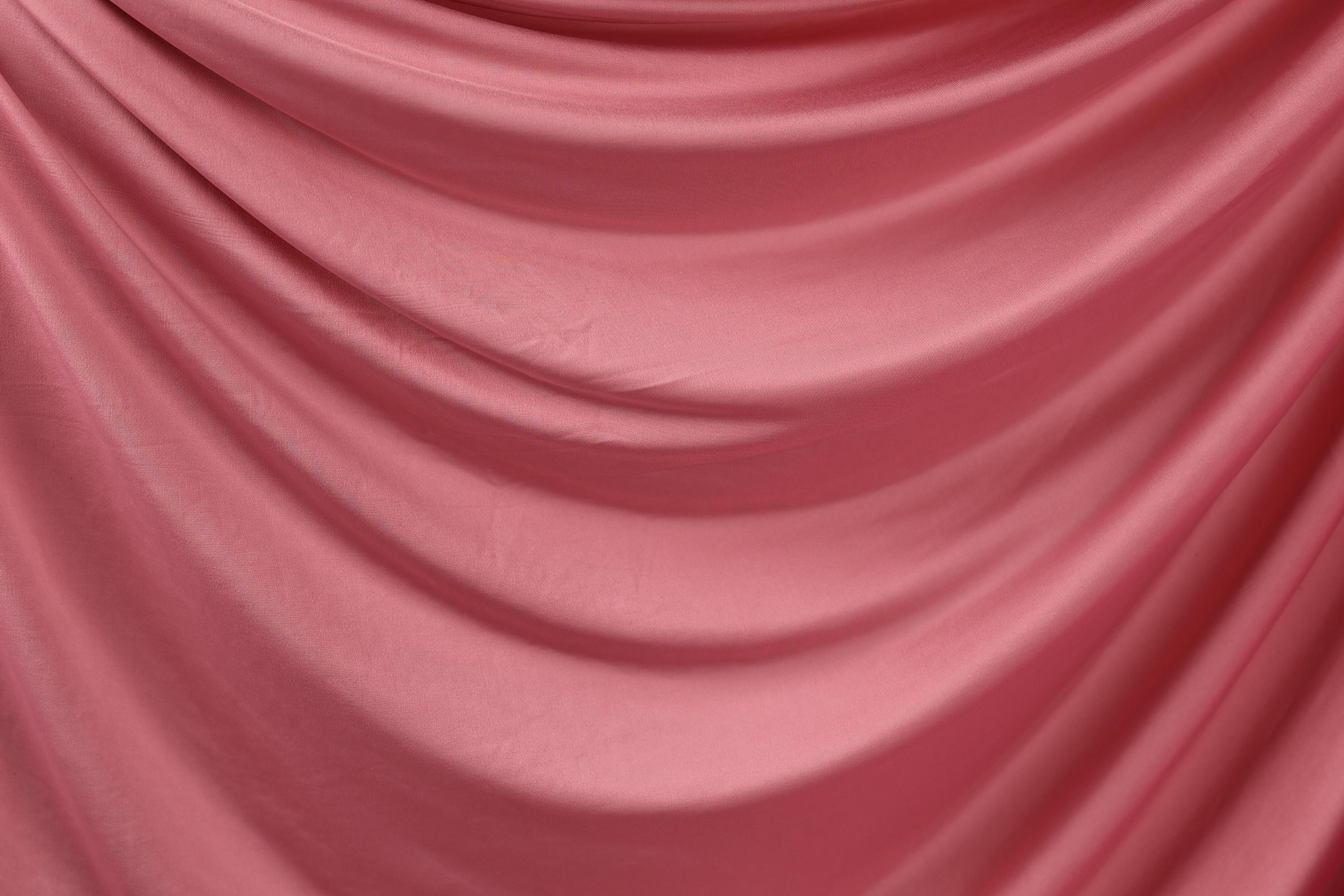a close-up view of a pink satin fabric, with its folds and creases creating a textured and flowing appearance.