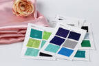 a collection of fabric swatches, each with a different color, laid out on a white surface. A pink satin fabric is visible in the background, and a single rose is placed next to the swatches.