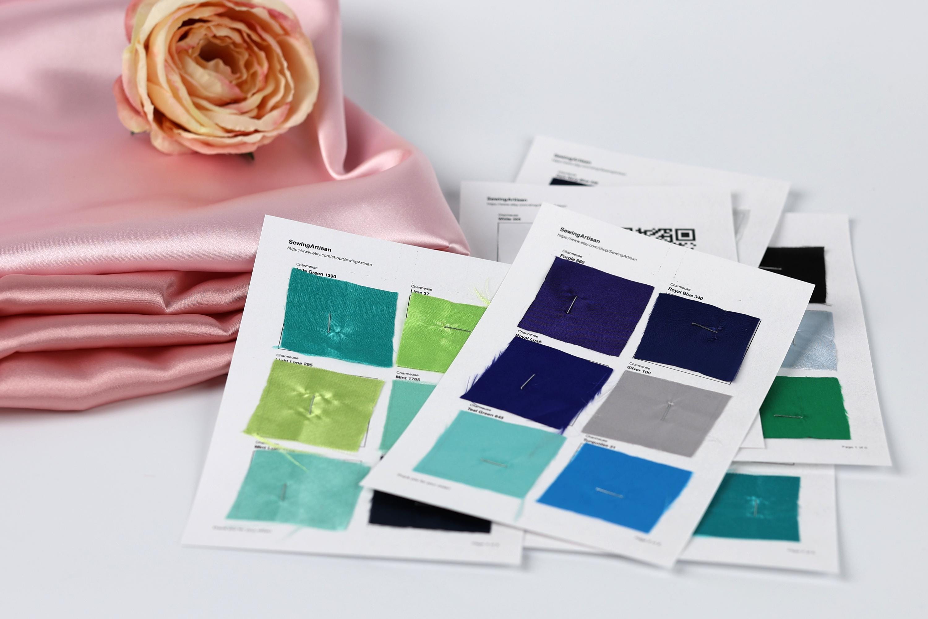 a collection of fabric swatches, each with a different color, laid out on a white surface. A pink satin fabric is visible in the background, and a single rose is placed next to the swatches.