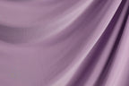 a close-up view of a soft, flowing purple fabric, possibly a satin or chiffon material. The fabric appears to be made of silk or a similar luxurious material, with a smooth and shiny texture. The image does not contain any discernible objects or actions, and the focus is solely on the fabric's texture and color.