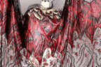 a dress with a striking red and black pattern, including sequins and lace elements. The dress appears to be a flowing, dramatic garment with a dramatic, fiery design.