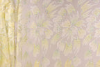 a close-up view of a fabric with a floral pattern, including yellow and white flowers and leaves. The fabric appears to be made of a shiny, glittery material, giving it a sparkly and eye-catching appearance.