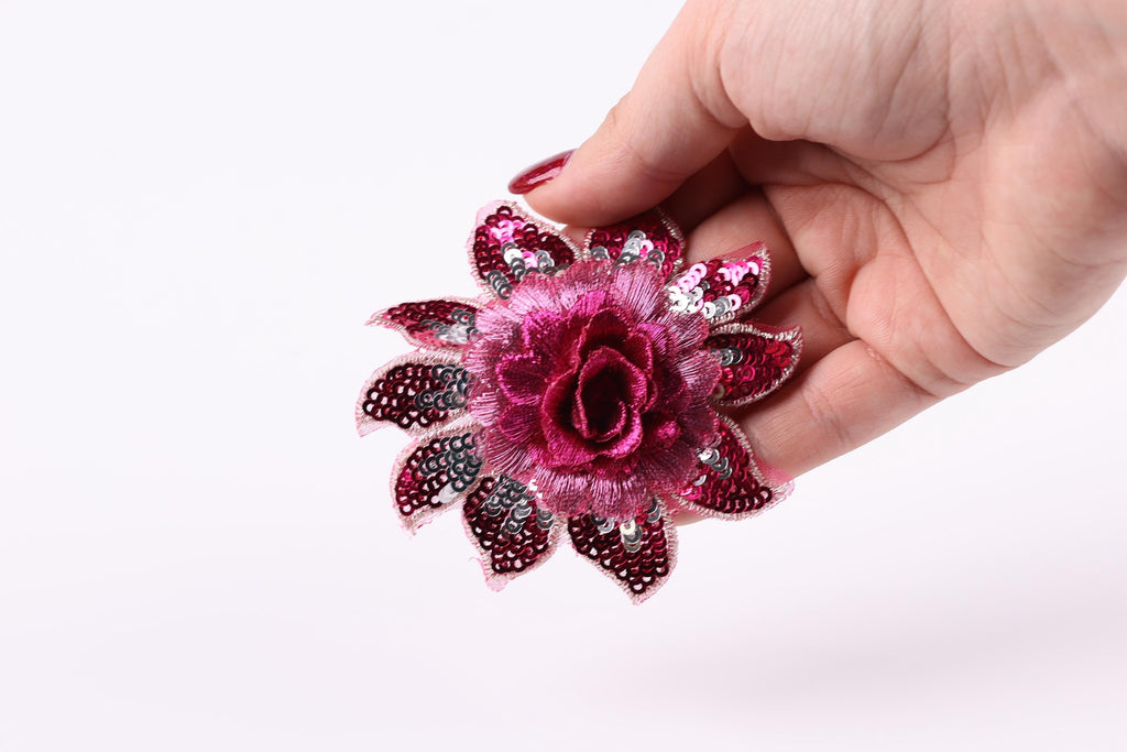 A hand holding a pink sequin flower against a white background.