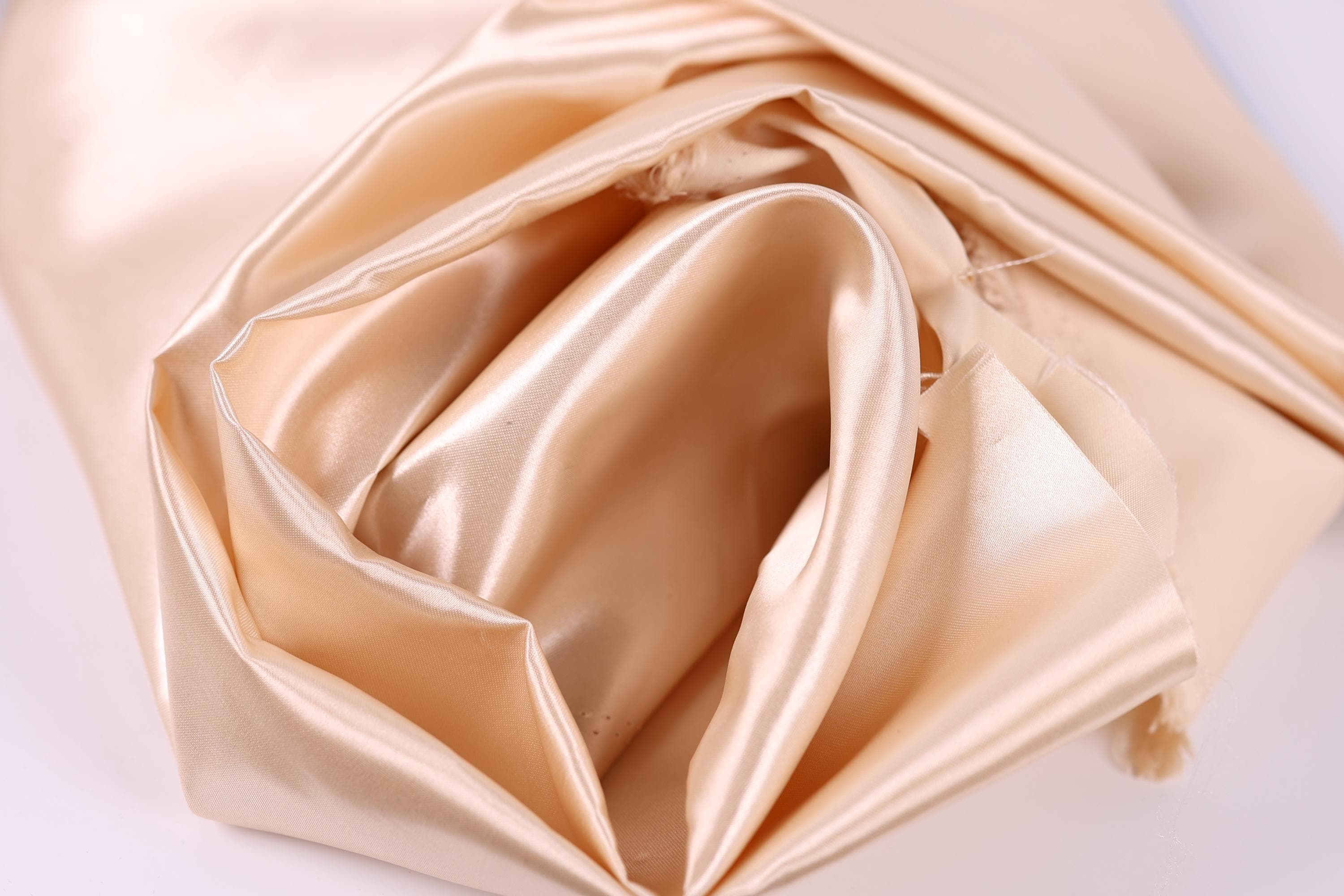 A close-up view of a soft, light-colored fabric, possibly silk or satin, with a smooth and shiny texture.