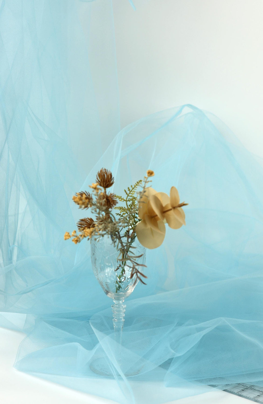 A clear glass vase filled with dried flowers and leaves sits on a blue fabric surface.