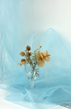 A clear glass vase filled with dried flowers and leaves sits on a blue fabric surface.