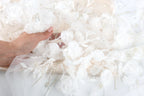 A hand is holding a piece of white fabric with delicate white flowers and leaves attached to it.