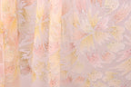 a close-up view of a fabric with a floral pattern in shades of pink and yellow. The fabric appears to be made of sheer material, with a delicate and intricate design.