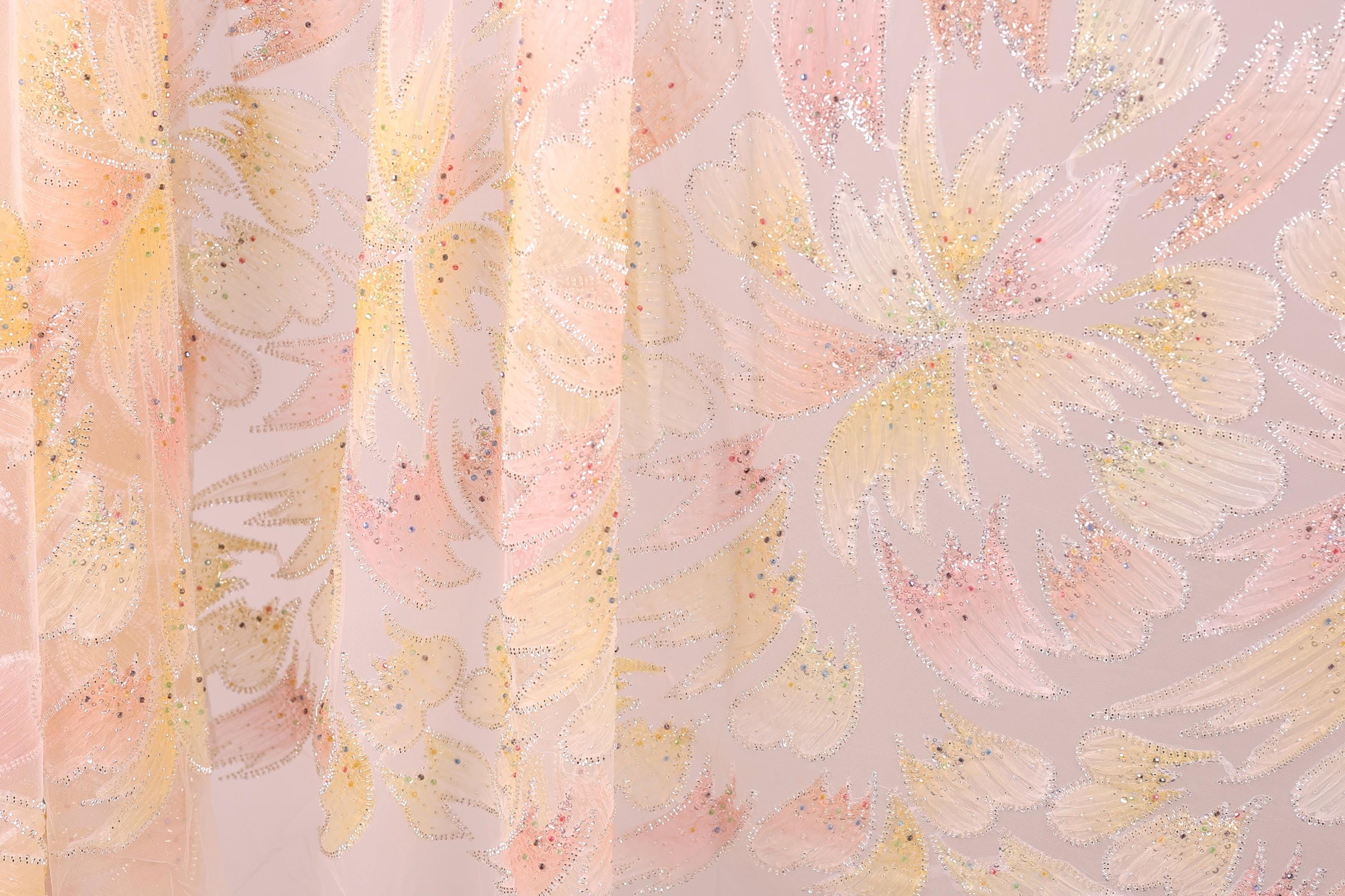 a close-up view of a fabric with a floral pattern in shades of pink and yellow. The fabric appears to be made of sheer material, with a delicate and intricate design.