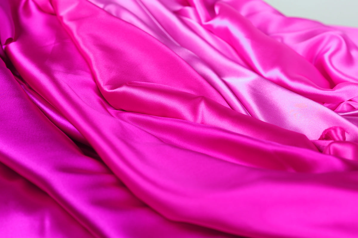 The image is a close-up of a fabric with a vibrant pink color, featuring a smooth and shiny texture.