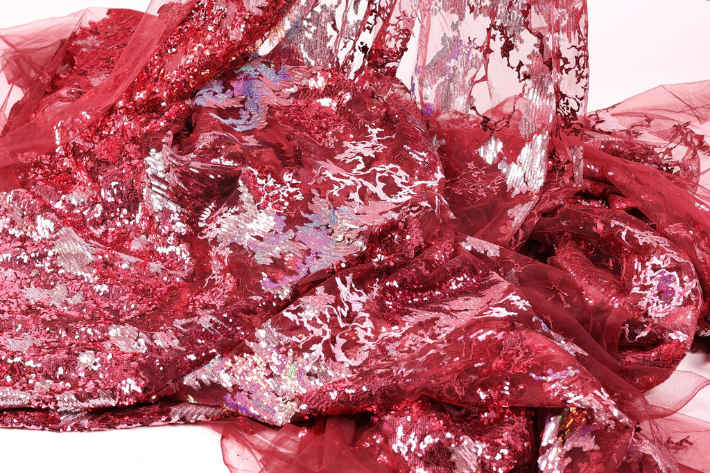 The image is a close-up of a red fabric with a floral pattern, featuring a mix of sequins and lace.
