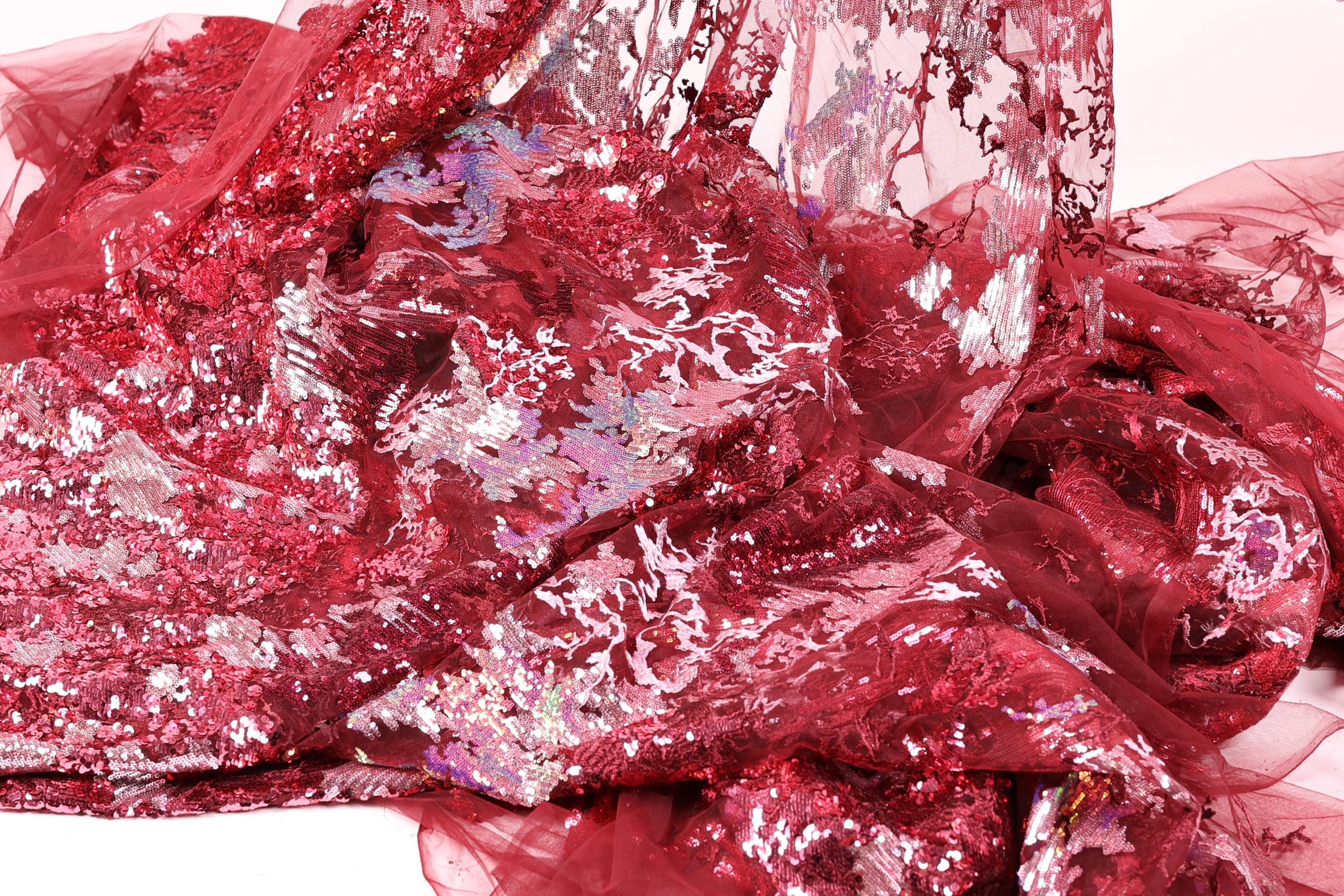 The image is a close-up of a red fabric with a floral pattern, featuring a mix of sequins and lace.