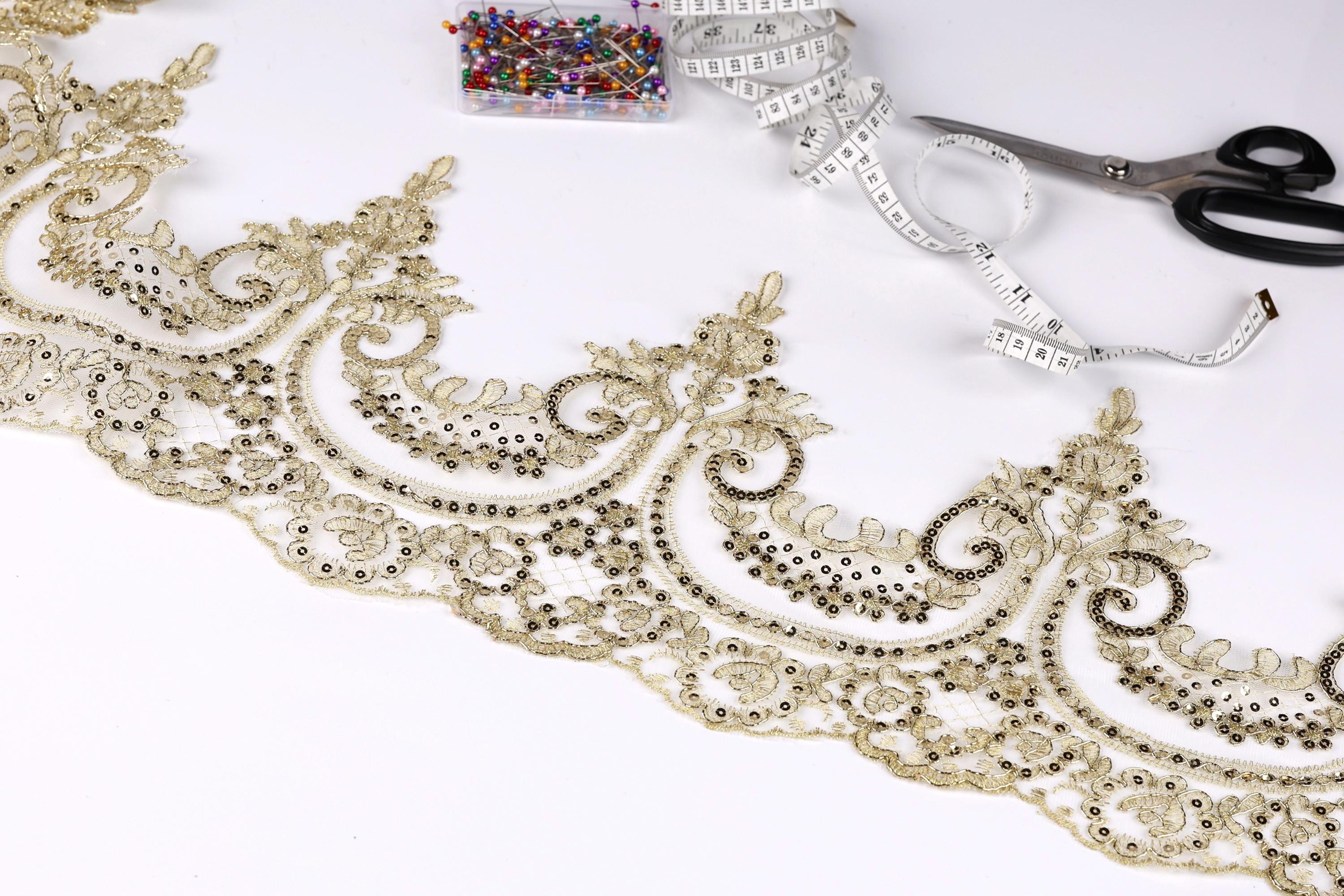 a close-up view of a decorative gold lace trim with intricate floral patterns, along with sewing tools such as scissors and a measuring tape.