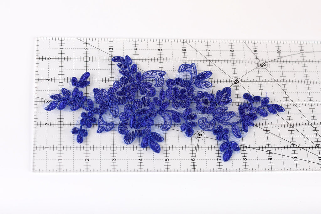 a clear ruler with blue floral embroidery pieces placed on it.