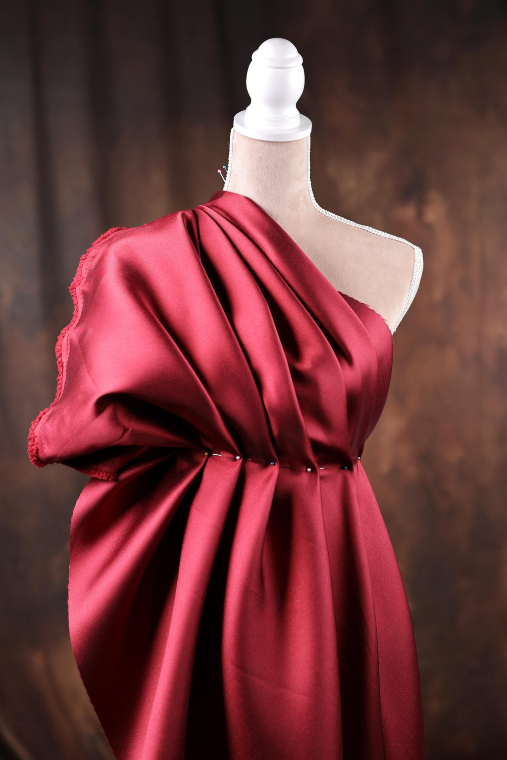A red one-shoulder dress displayed on a mannequin, with a dark background.