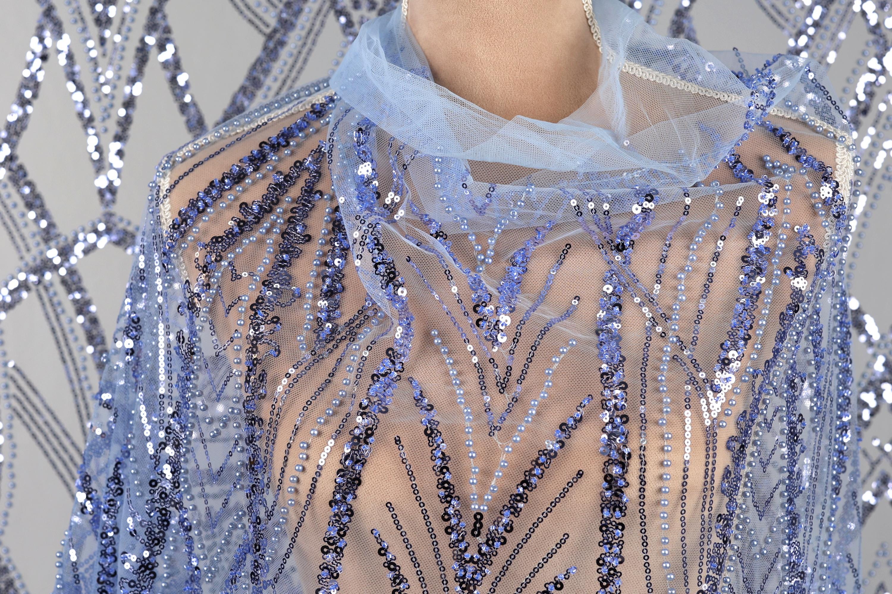 A close-up view of a person wearing a blue sequined dress with a sheer overlay.