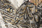 The image is a close-up of a fabric with a black and gold pattern, featuring a lot of sequins and glitter.
