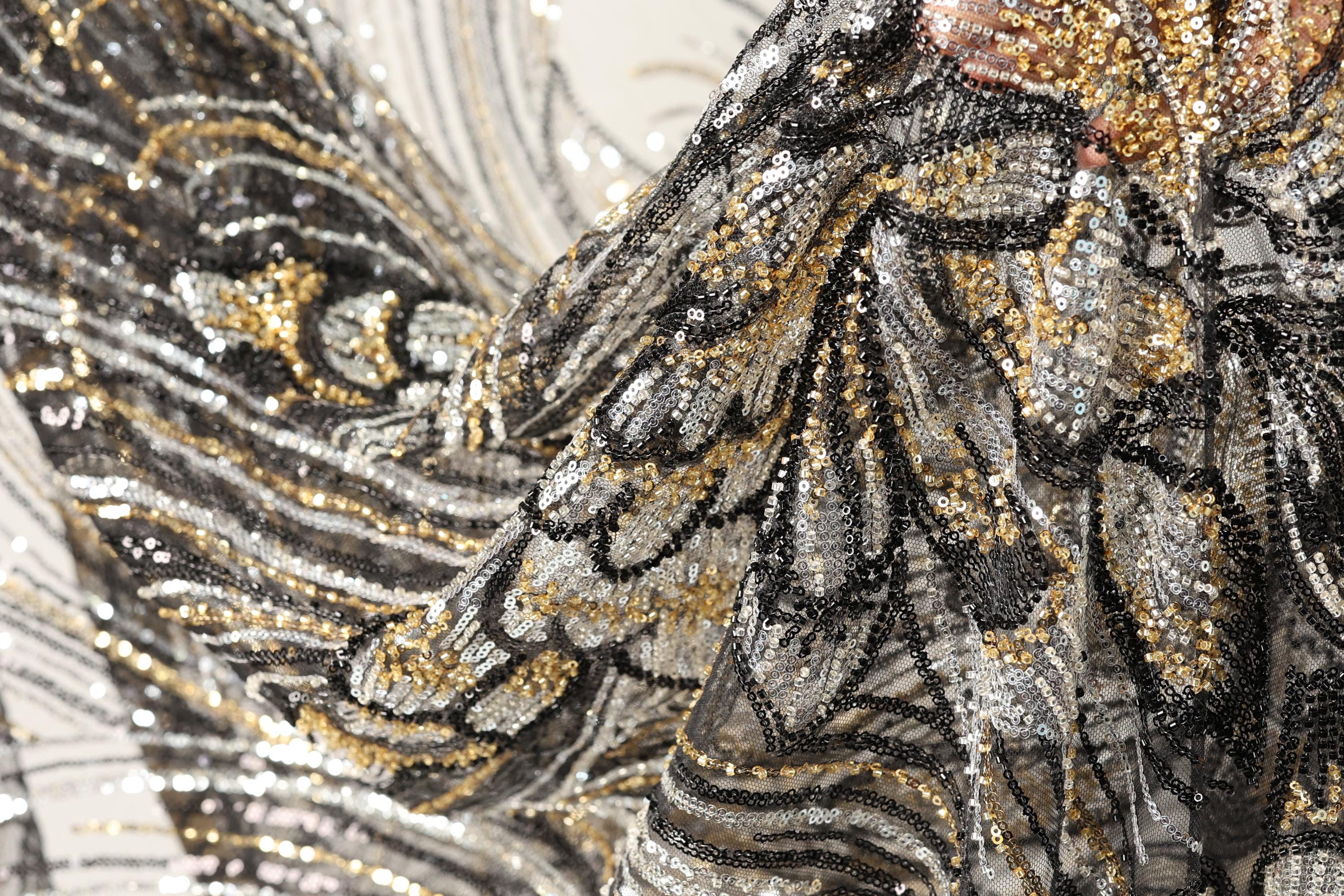 The image is a close-up of a fabric with a black and gold pattern, featuring a lot of sequins and glitter.