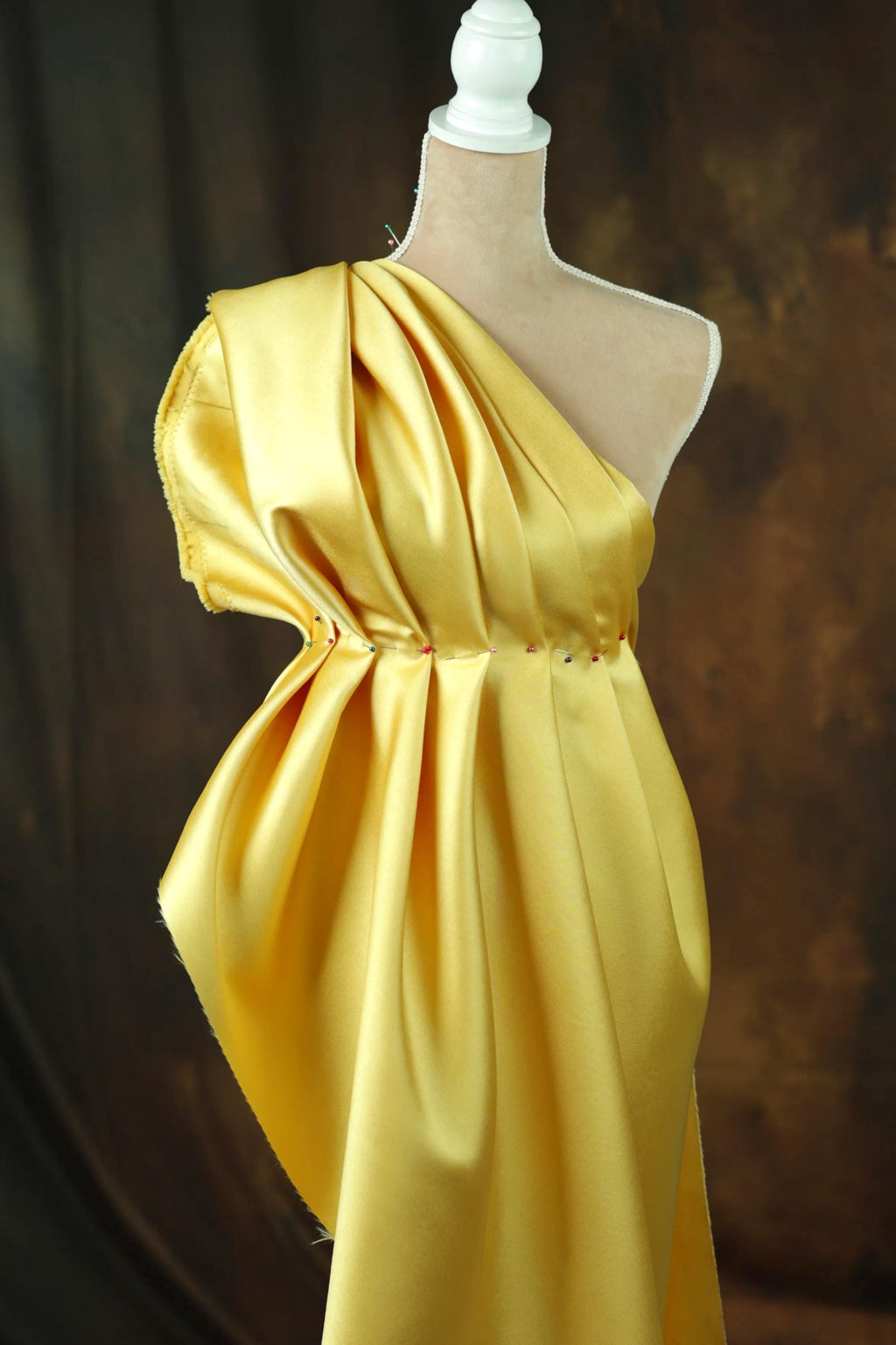 A mannequin wearing a yellow one-shoulder dress with a draped, flowing silhouette.