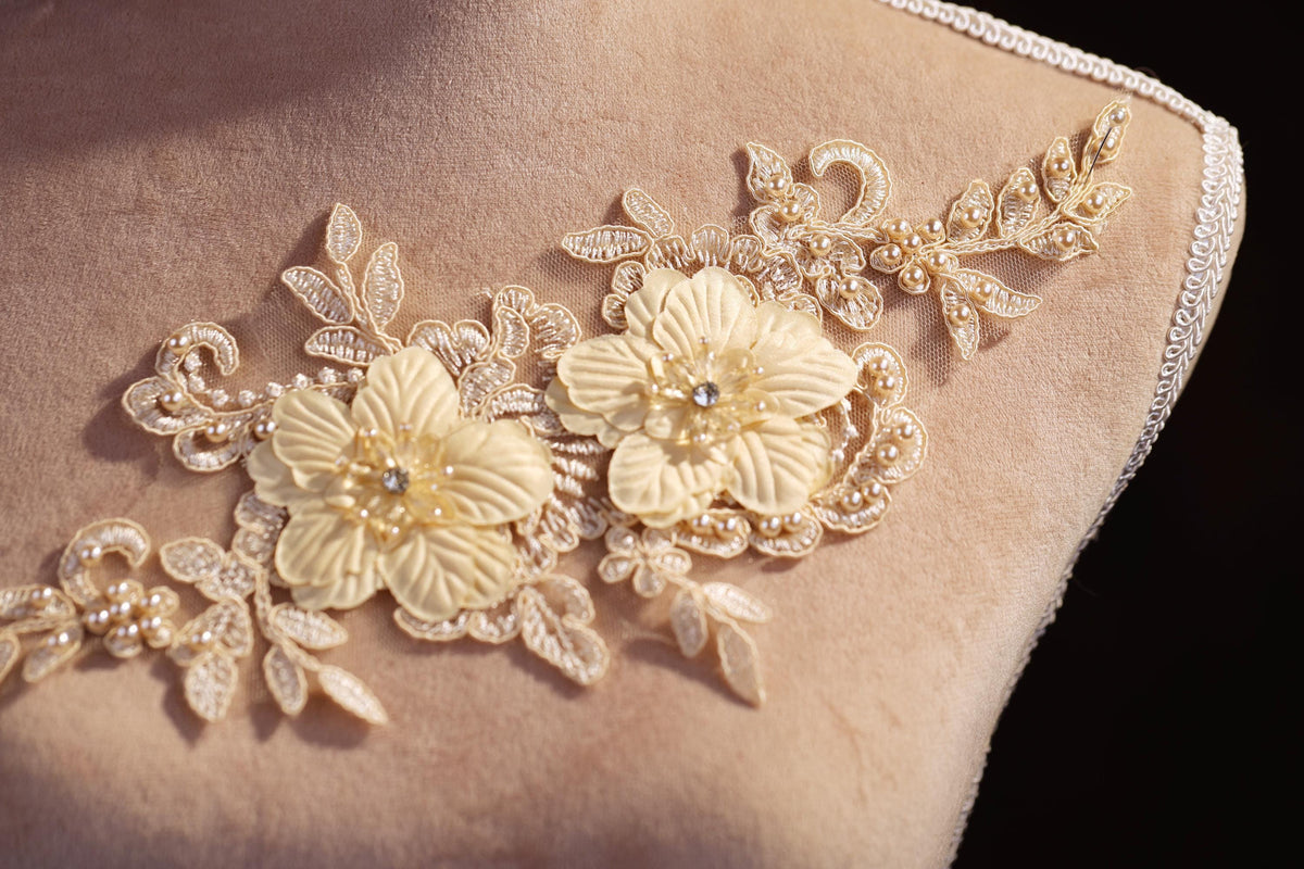 A close-up image of a delicate, beige lace flower embroidery on a fabric, with intricate details and a floral pattern.