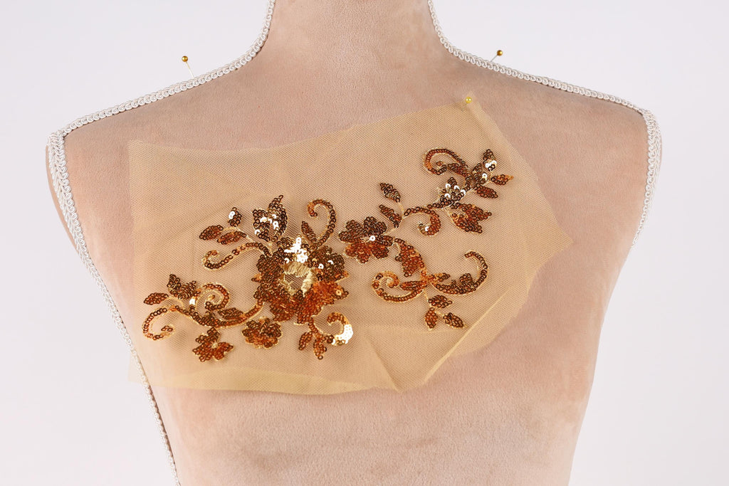 a mannequin torso with a beige fabric piece featuring a floral design and sequin embellishments.