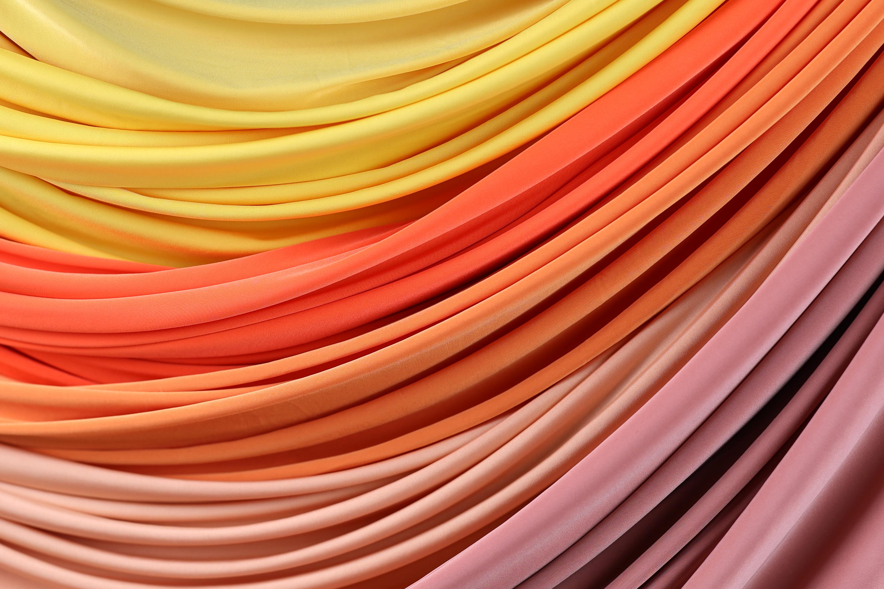 a close-up view of a vibrant arrangement of colorful fabric swatches, showcasing a gradient of warm hues from yellow to pink.