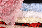 A close-up image of various colorful fabric swatches, including pink, white, blue, and red, with intricate patterns and embellishments.