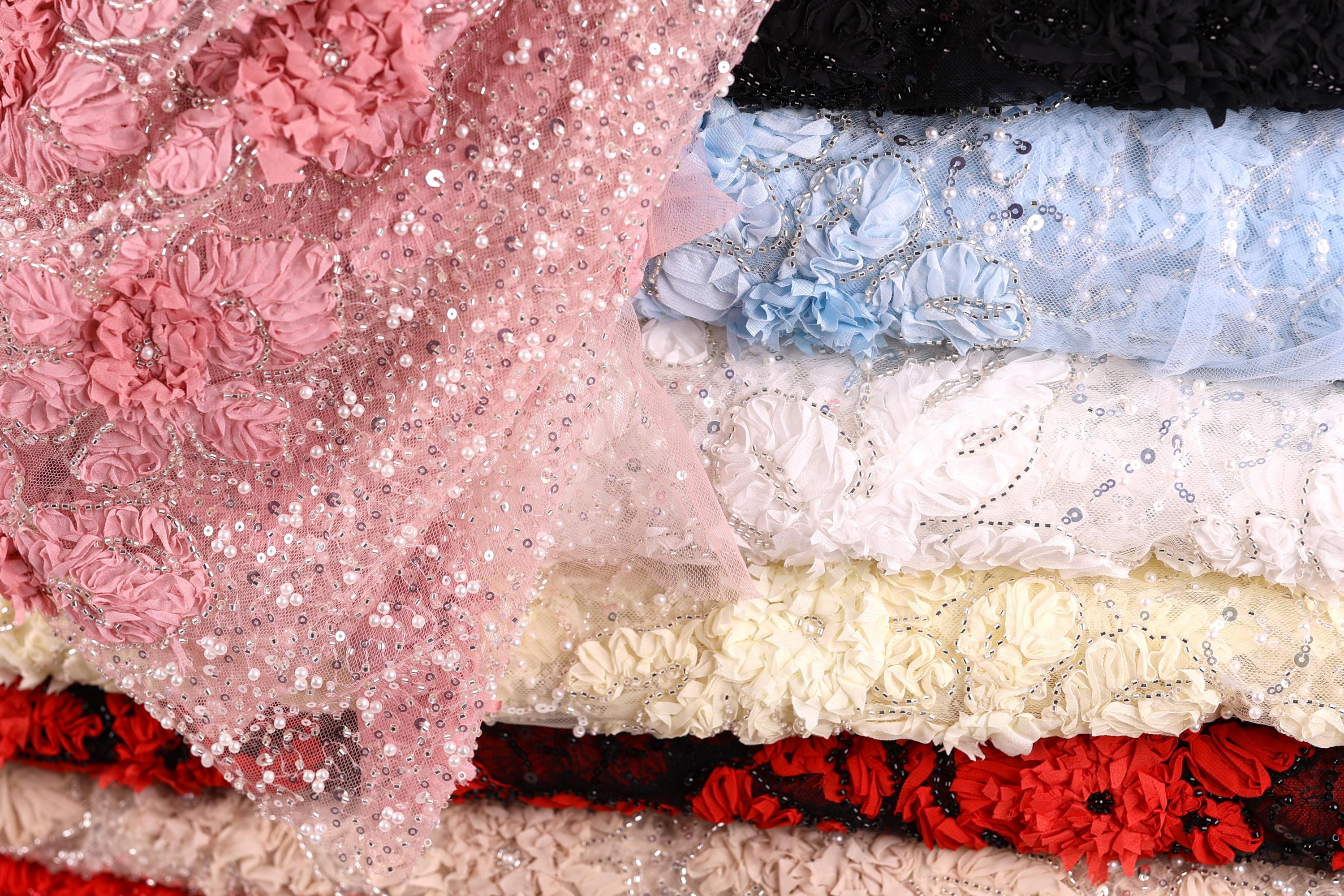 A close-up image of various colorful fabric swatches, including pink, white, blue, and red, with intricate patterns and embellishments.