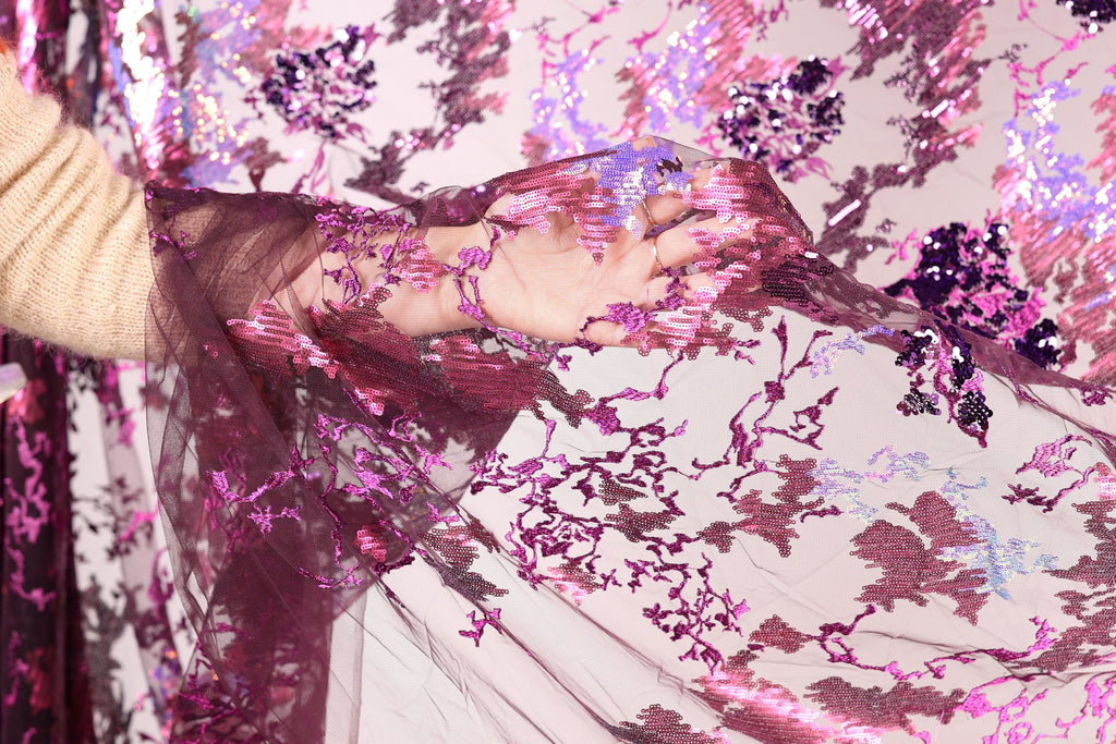 A hand is holding a piece of fabric with a floral pattern in shades of pink and purple.