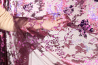 A hand is holding a piece of fabric with a floral pattern in shades of pink and purple.