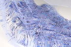 a close-up view of a fabric with a blue and purple floral pattern, featuring sequins and beads. The fabric appears to be a sheer material, with a delicate and intricate design.