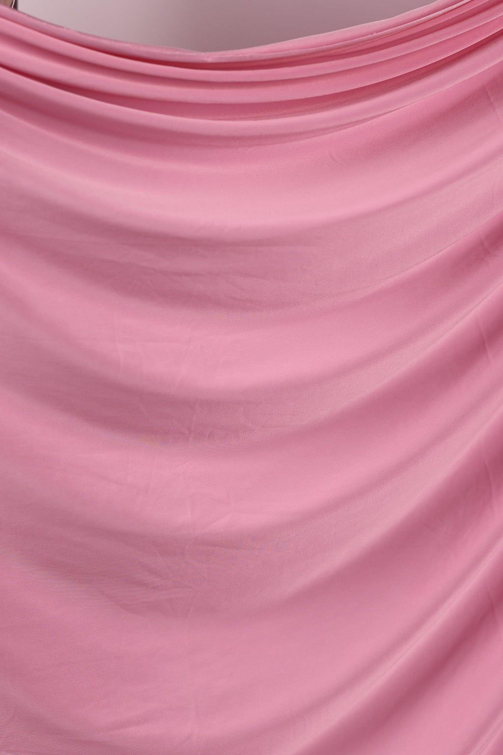 The image is a close-up of a pink fabric with a wavy texture, creating a soft and flowing appearance.