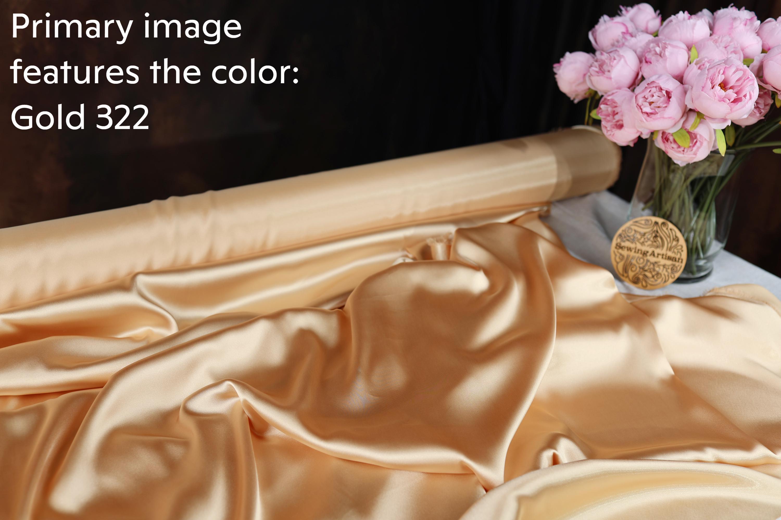 a roll of gold fabric with a vase of pink roses and a gold medal on a table.