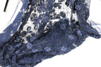 a close-up view of a fabric with a floral pattern, featuring blue and purple colors. The fabric appears to be made of lace or a similar material, with a delicate and intricate design.