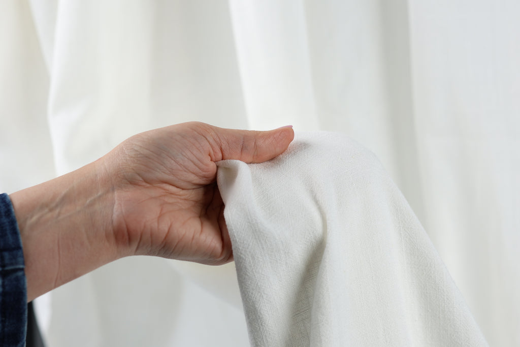 A hand is holding a white fabric, possibly a piece of clothing, against a white background.