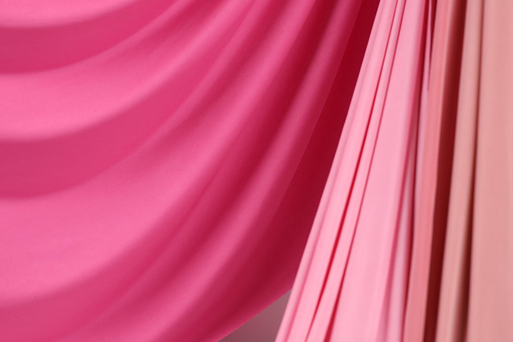 a close-up view of a vibrant pink fabric, with a subtle pink and orange striped pattern. The fabric appears to be soft and flowing, creating a visually appealing contrast against the background.